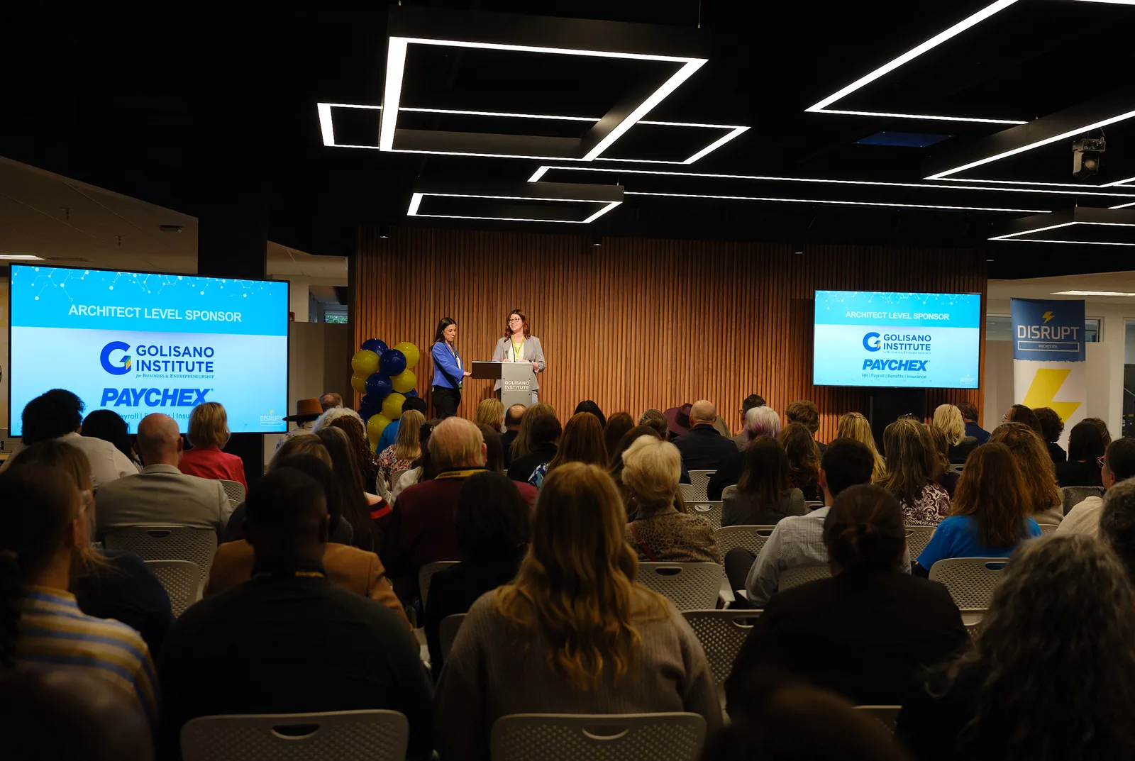 Disrupt Rochester — full audience with dual sponsor screens and live speakers